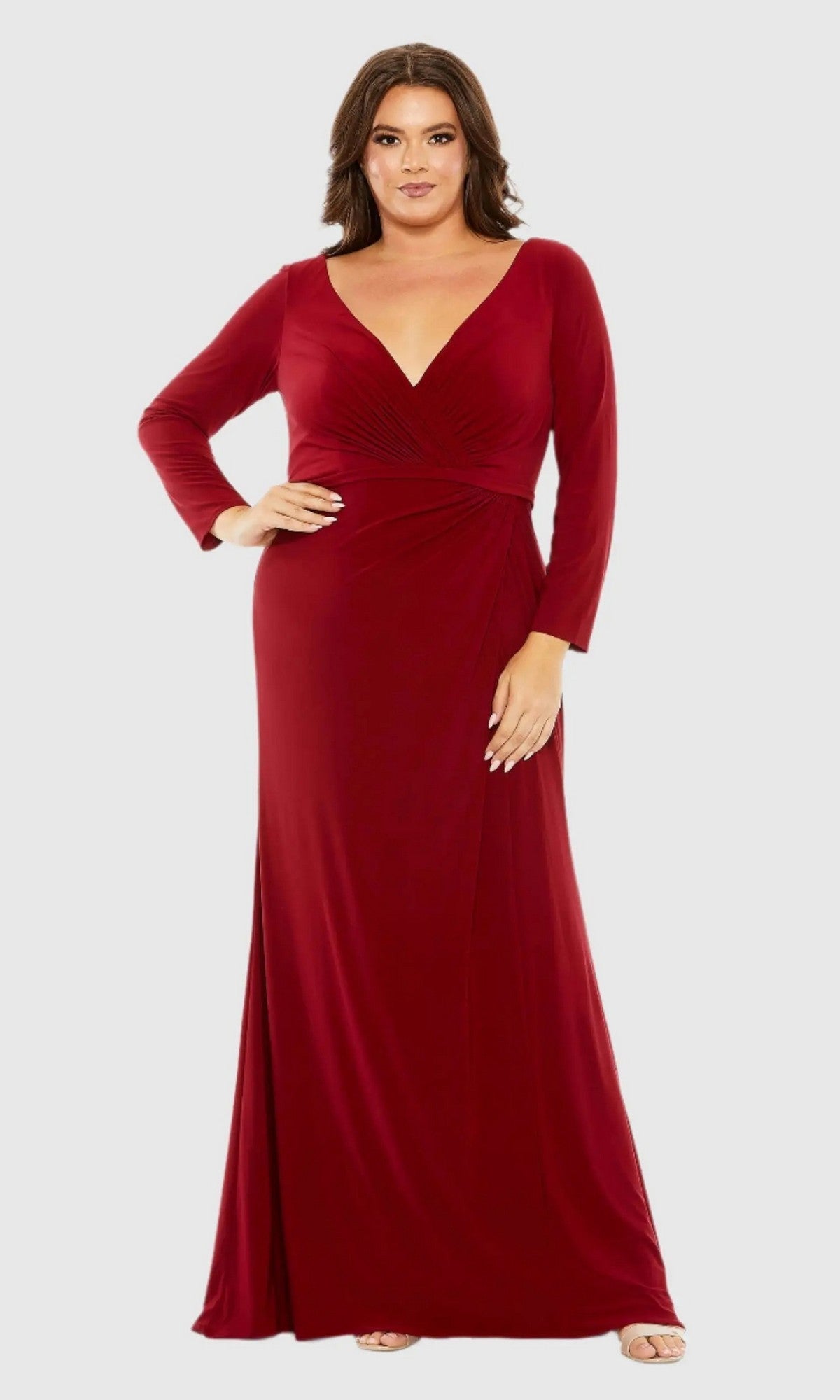 A woman models the Long Plus-Size Formal Dress 68442 by Mac Duggal, featuring a deep red v-neckline and long sleeves, standing against a plain light gray background.